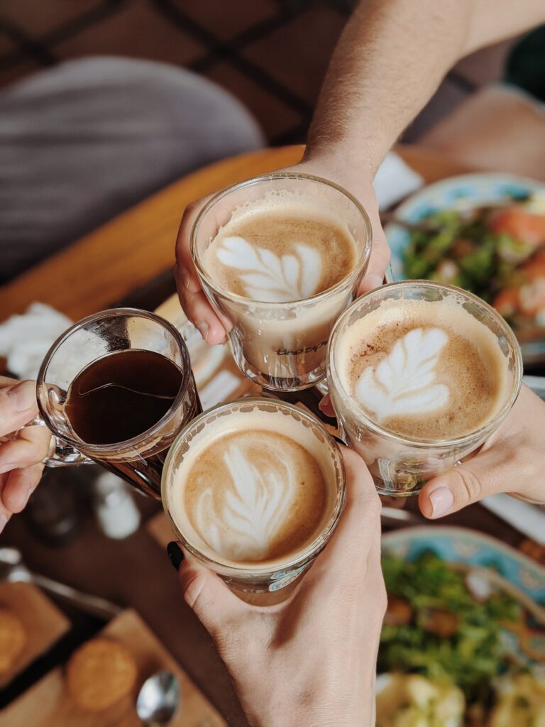 Four individuals holding coffee cups and joining hands together.